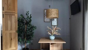 Une pièce avec un meuble en bois, une plante en pot, une table sur laquelle se trouve une lampe en osier, et un tableau encadré accroché au mur.