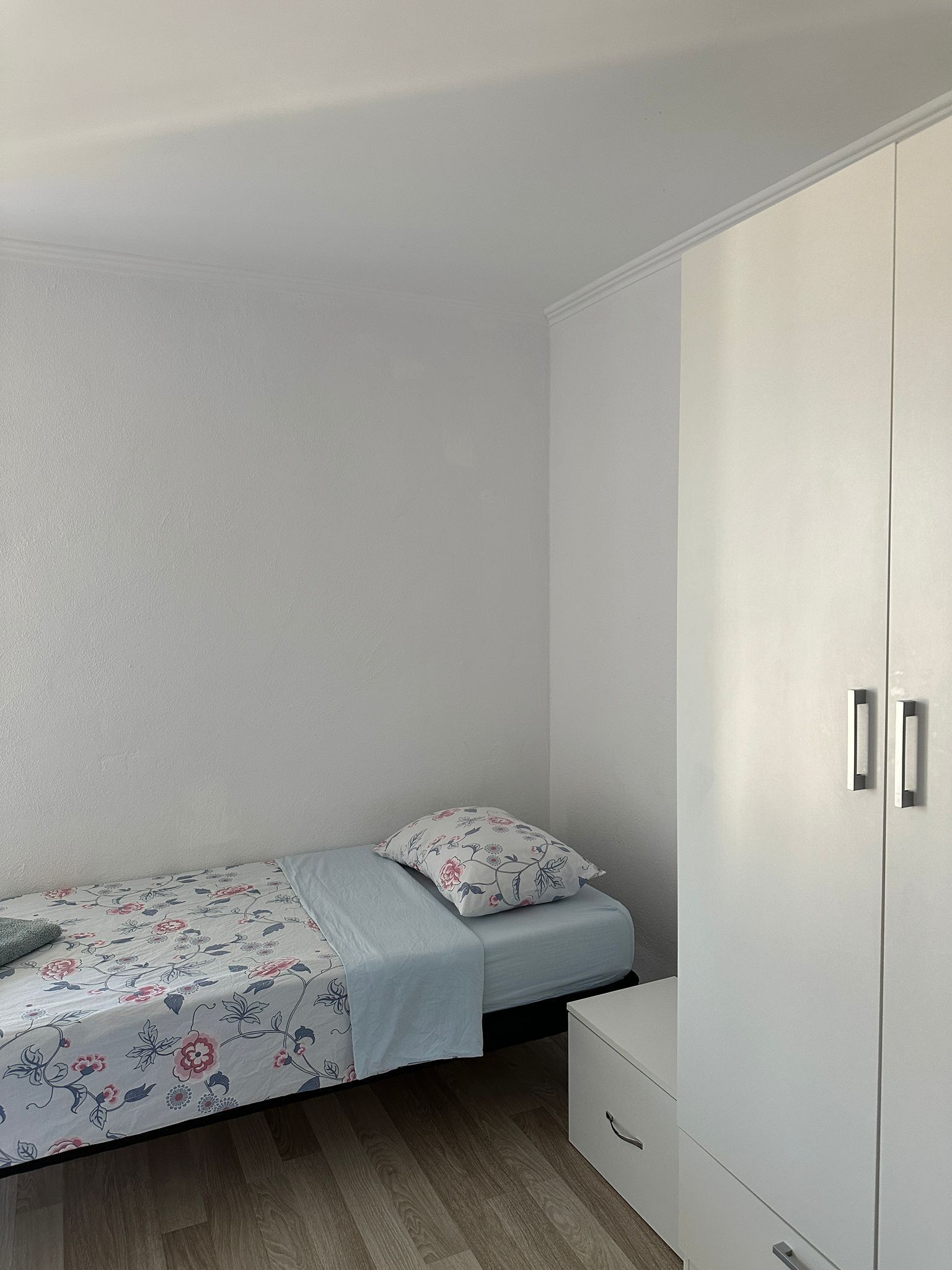 A small, neatly arranged bedroom with a single bed, a bedside table, and a wardrobe.