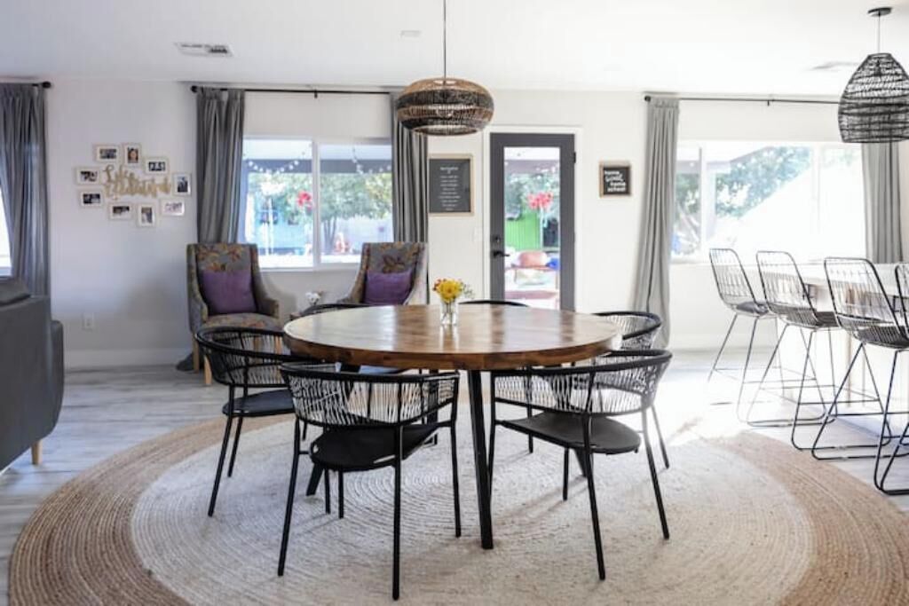 A modern dining area with a round wooden table surrounded by black wire chairs, a woven rug, and pendant lighting.