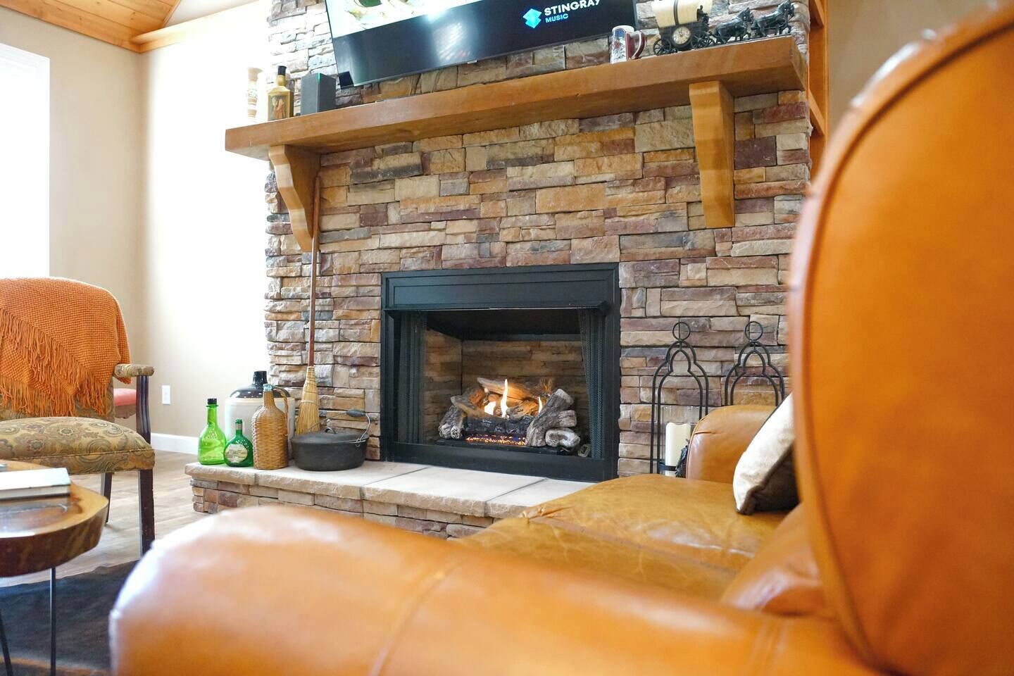A living room with a stone fireplace, a leather sofa, and a television mounted above the fireplace.