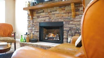 A living room with a stone fireplace, a leather sofa, and a television mounted above the fireplace.