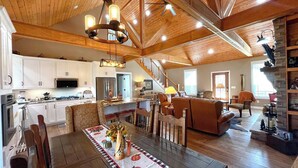 A spacious living area with a high ceiling, wooden beams, a dining table with a decorative runner, and a cozy seating arrangement.