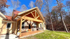 A wooden cabin with a porch, stone walls, and a red roof.