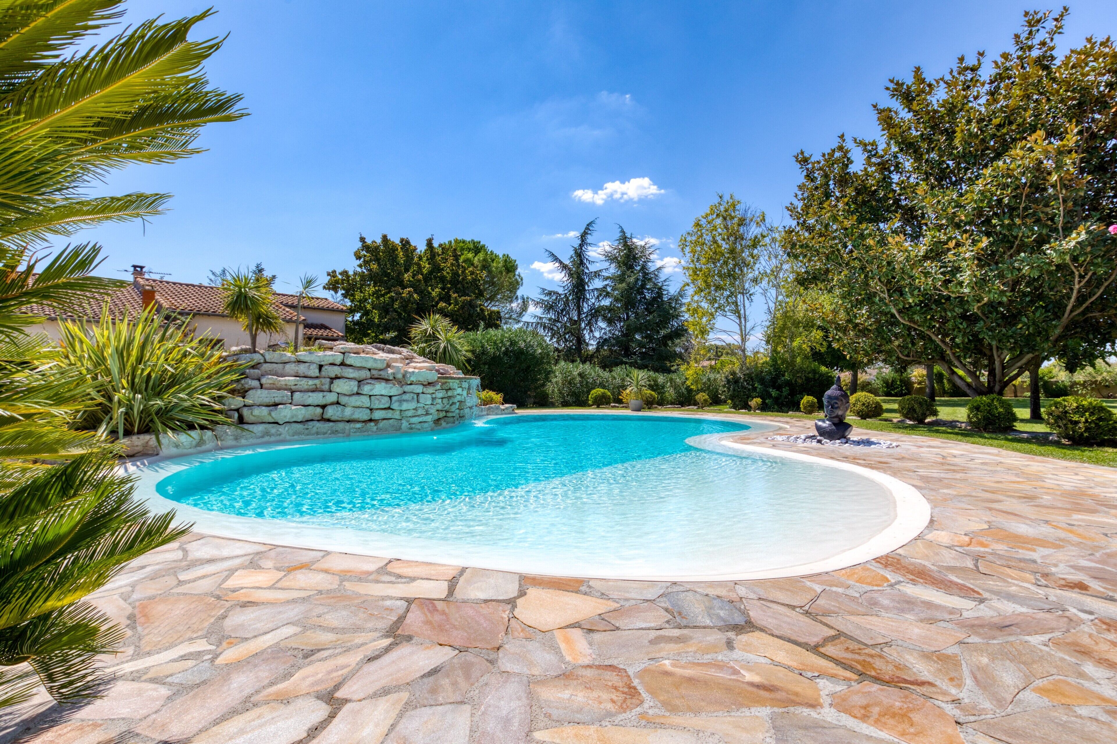 A swimming pool with a stone border, surrounded by greenery and a stone wall.