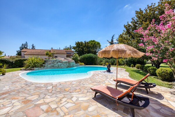 A swimming pool with stone tiles, lounge chairs, and a thatched umbrella. - Country House 'L'évaroma' with Private Pool, Wi-Fi and Air Conditioning (Campagne)