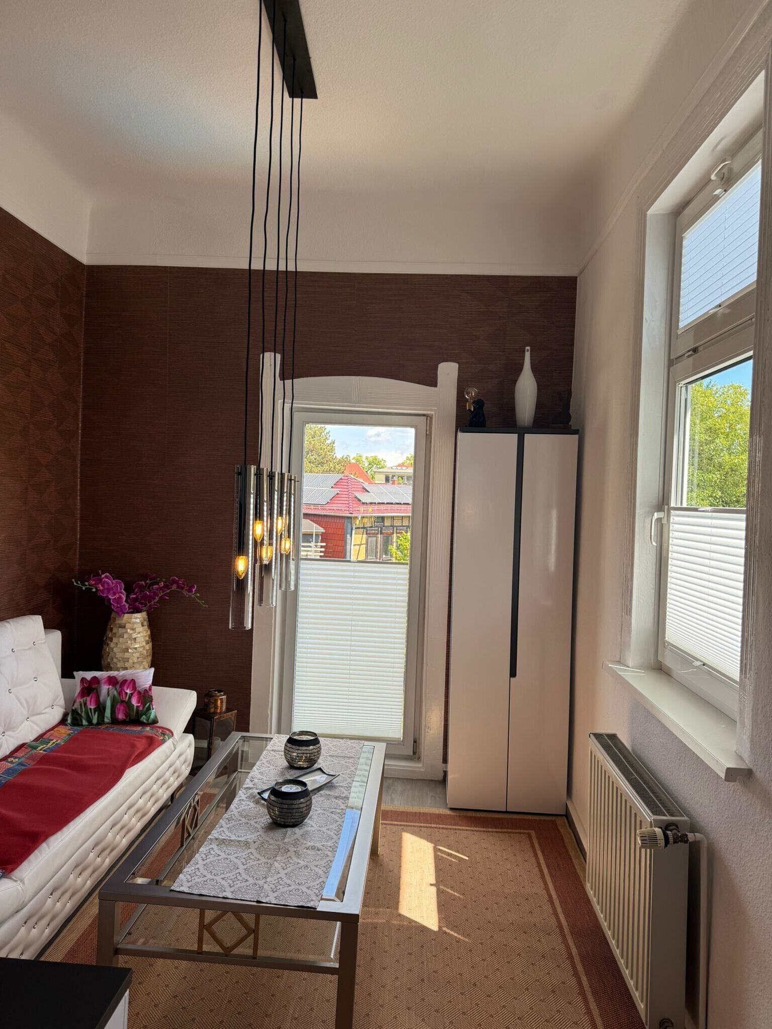 Ett modernt kök med ett kylskåp, ett matbord med en vas och en soffa med en röd filt.