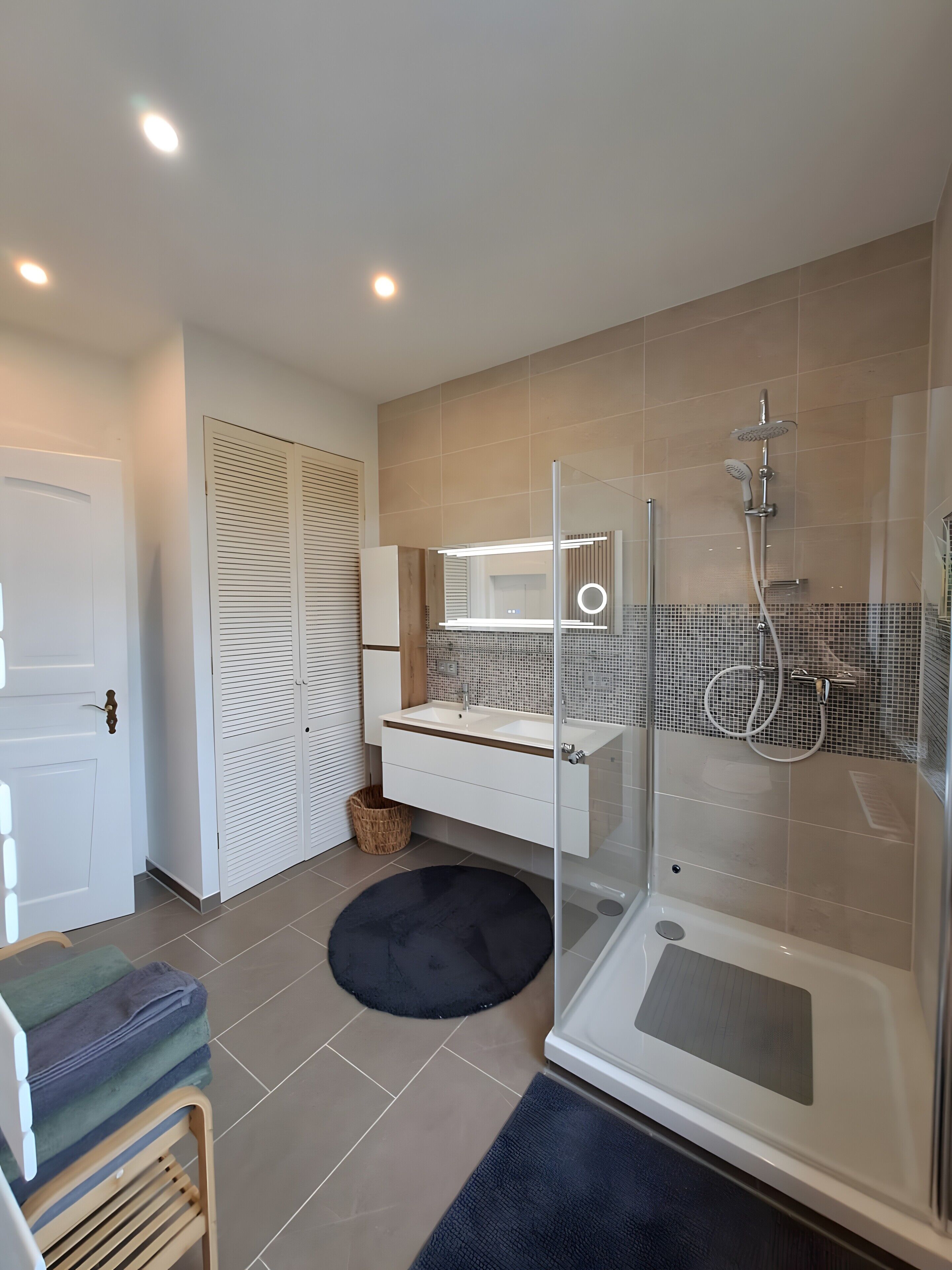Une salle de bain moderne avec une douche à parois de verre, un meuble-lavabo avec un miroir et un petit tapis rond sur le sol.
