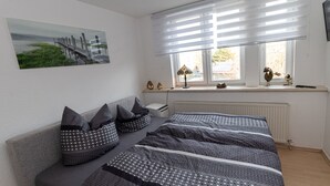 Een slaapkamer met een bed, een raam met zonwering, een radiator en een aan de muur hangend schilderij.