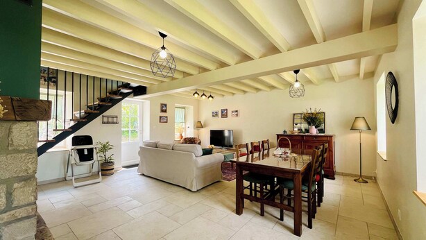 A spacious living area with a dining table and chairs, a sofa, a staircase, and a fireplace. - Les Chatons - Gite au coeur de la campagne (Fresville)
