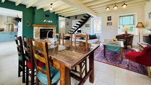 A spacious living area with a wooden dining table, chairs, a fireplace, a staircase, and a cozy seating area with a red chair. - Les Chatons - Gite au coeur de la campagne (Fresville)