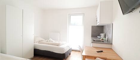 A small, bright room with a bed, a desk, and a TV.