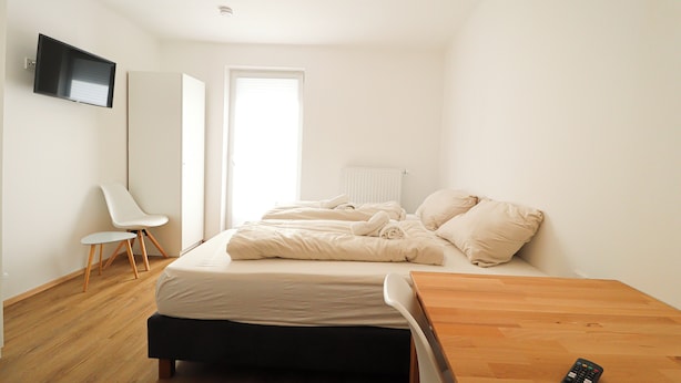 A bedroom with a bed, a desk, a chair, a TV, and a window. - Pöckau 32 Smart Rooms Self Check In (Arnoldstein)