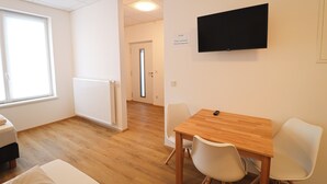 A room with a wooden table, two white chairs, a bed, a radiator, a window, and a TV mounted on the wall. - Pöckau 32 Smart Rooms Self Check In (Arnoldstein)