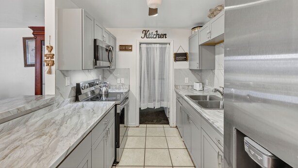A modern kitchen with white cabinets, stainless steel appliances, and a ceiling fan. - Spacious home with 7 beds, home gym, office with oversized backyard. (Fort Myers)