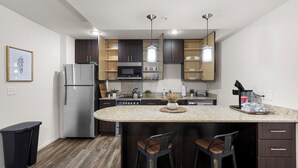 A modern kitchen with a central island, dark cabinetry, stainless steel appliances, and pendant lighting.
