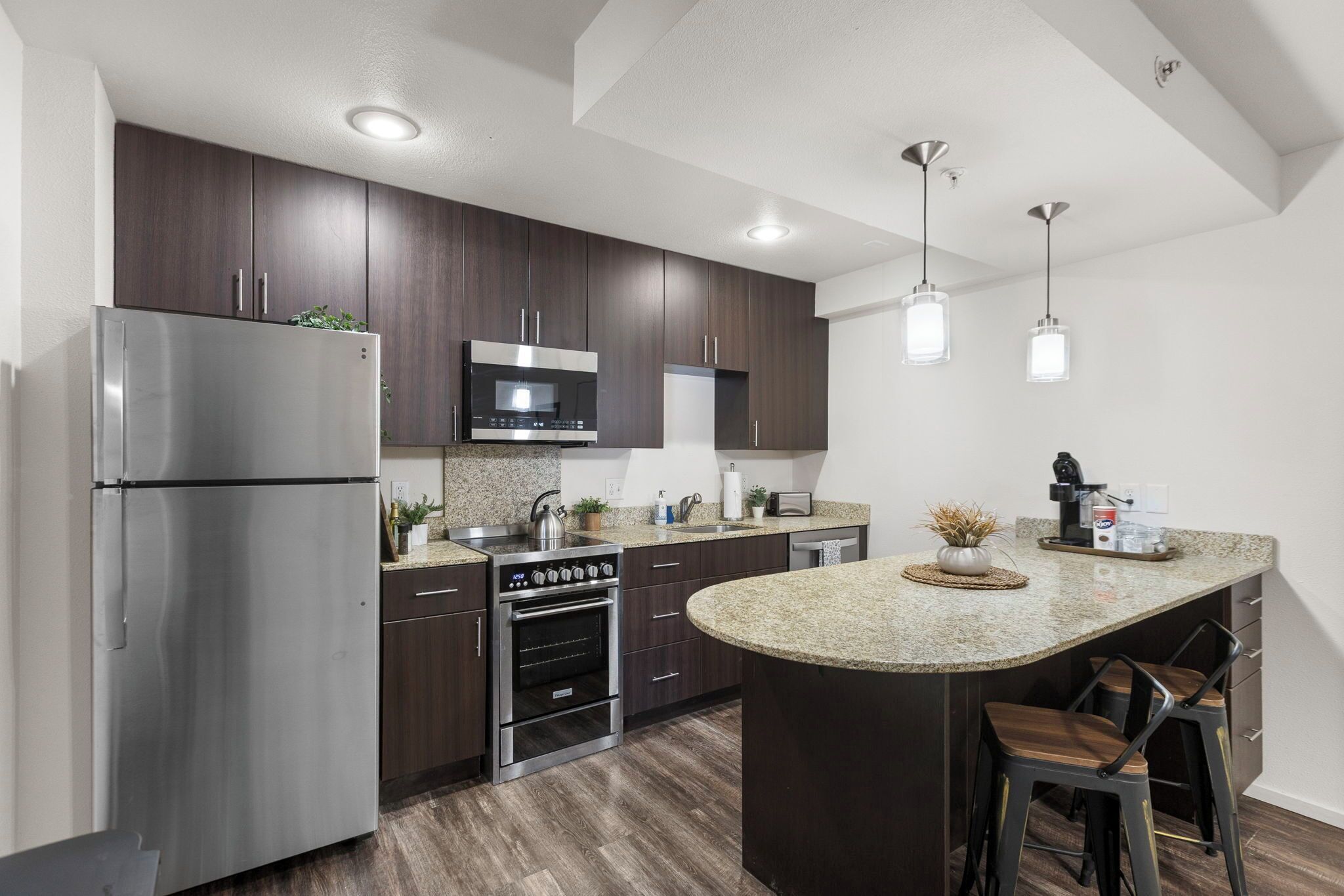 A modern kitchen with dark wood cabinets, stainless steel appliances, granite countertops, and a central island with bar stools.