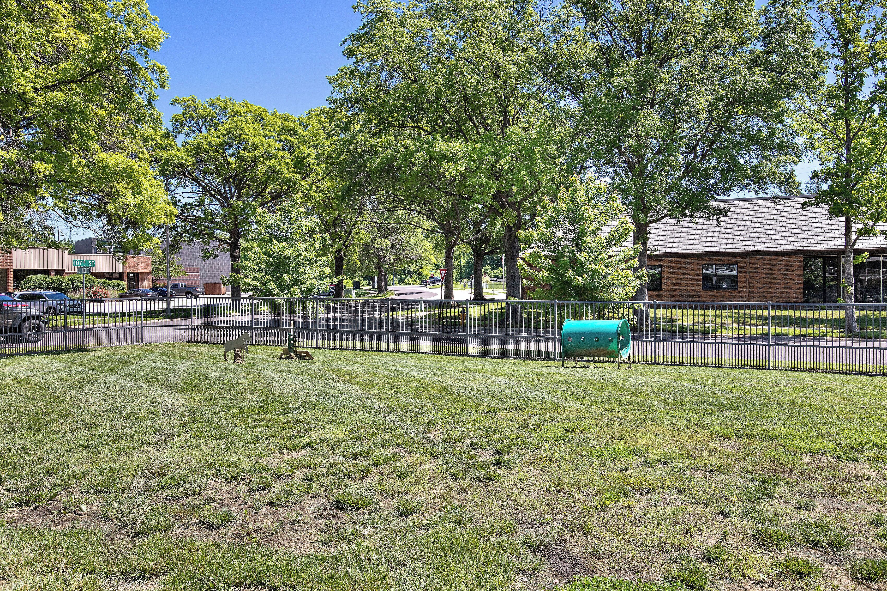 A grassy area with a fence, trees, and a building in the background.