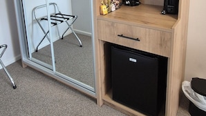 Quarto compacto com uma escrivaninha de madeira, um frigorífico preto, micro-ondas e uma máquina de café pequena.