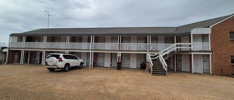 A two-story motel with a covered front porch, a staircase to the upper level, and a gravel driveway.