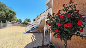 Um edifício com fachada de tijolos, escadaria que leva a um andar superior e um jardim com rosas vermelhas.
