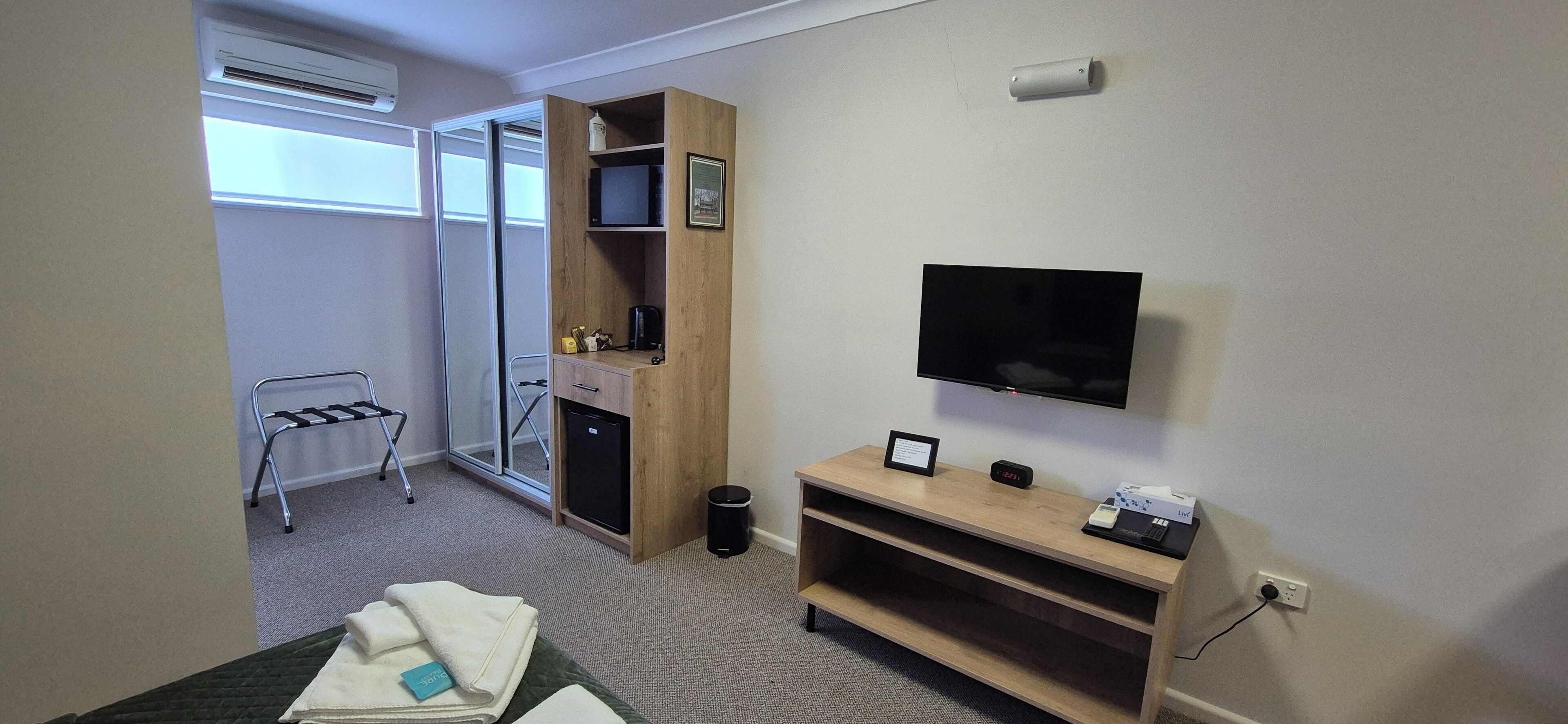 Een hotelkamer met een bed, een bureau met een computer, een aan de muur bevestigde televisie, een klein kastje en een raam met uitzicht.