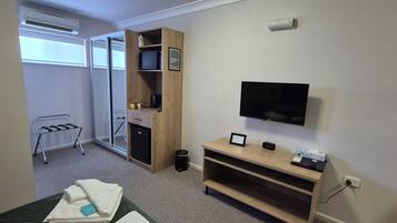 Een hotelkamer met een bed, een bureau met een computer, een aan de muur bevestigde televisie, een klein kastje en een raam met uitzicht.
