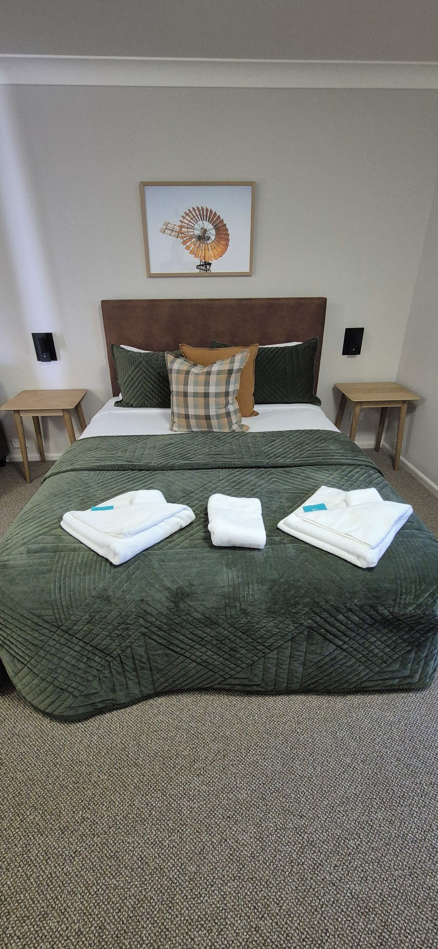 A neatly made bed with a green quilt, two pillows, and three folded towels.