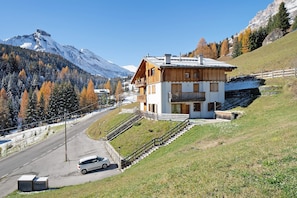 A two-story chalet with a balcony, a staircase, and a view of a mountain.