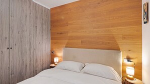 A bedroom with a wooden headboard, a bed with white bedding, two bedside lamps, and a nightstand. - Apartment 'Sunny Arabba' with Mountain View, Private Garden and Wi-Fi (Arabba)