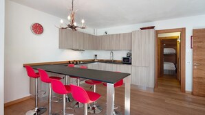 A modern kitchen with a central island, red bar stools, a chandelier, and a clock on the wall. - Apartment 'Sunny Arabba' with Mountain View, Private Garden and Wi-Fi (Arabba)