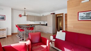 A modern living room with red furniture, a kitchen with light wood cabinets, and a dining area with red chairs. - Apartment 'Sunny Arabba' with Mountain View, Private Garden and Wi-Fi (Arabba)