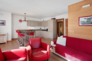 Una sala de estar moderna con muebles rojos, una cocina con armarios de madera clara y un comedor con sillas rojas.