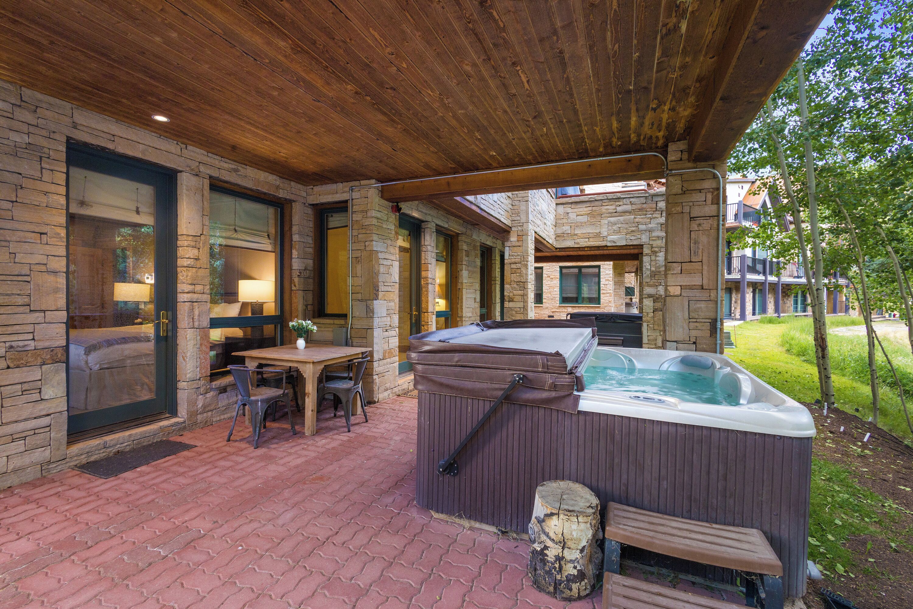 A covered patio area with a hot tub, stone walls, and a wooden ceiling.