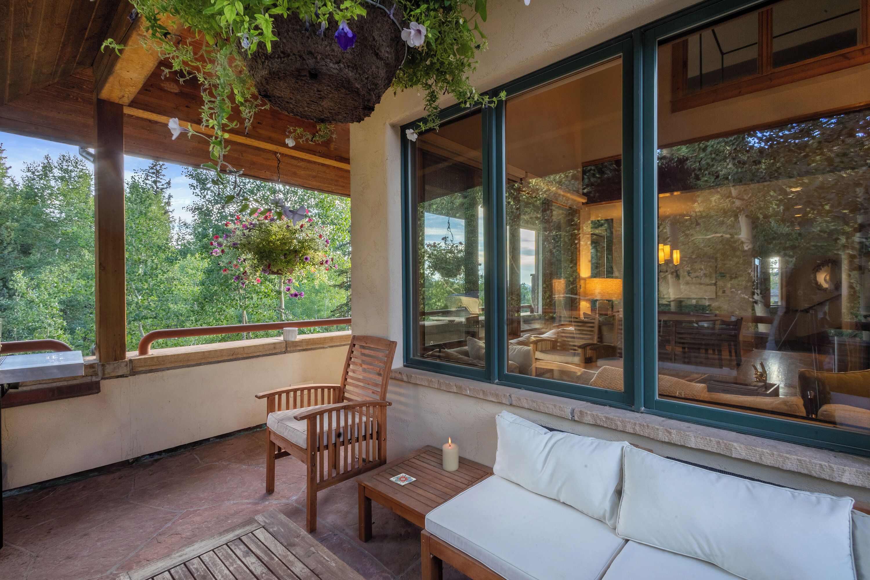 Una terraza de madera con un sofá y sillas, una planta colgante y vistas al exterior.