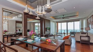 A spacious living area with a wooden dining table, multiple seating options, and large windows offering a view of the outdoors. - Shasa Vela Condominium B, Mared, Koh Samui (Koh Samui)