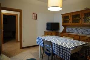 A small kitchen with a dining table, chairs, a television, wooden cabinets, and a tiled backsplash.