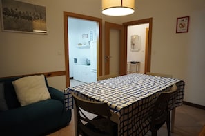 A room with a dining table, a sofa, and a kitchen area visible through an open door.