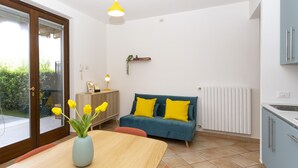 Eine moderne Küche mit Essbereich, ein blaues Sofa mit gelben Kissen und ein Holztisch mit einer Vase voller gelber Blumen.