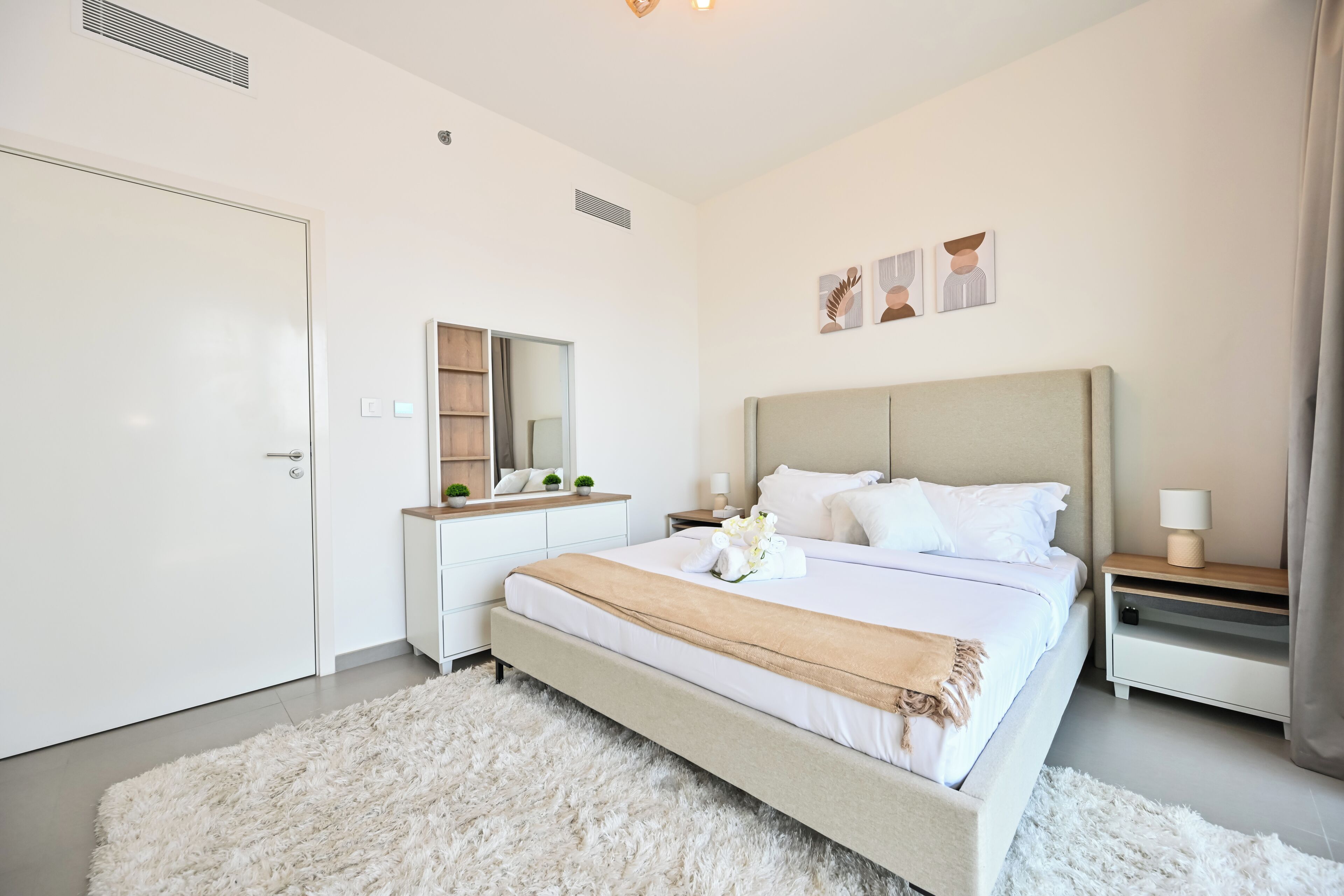 Un dormitorio moderno con una cama grande, una mesita de noche con lámpara, un aparador y un espejo.