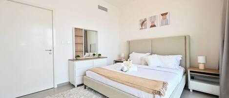 Un dormitorio moderno con una cama grande, una mesita de noche con lámpara, un aparador y un espejo.