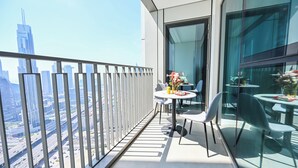 A balcony with a glass railing, a round table with chairs, and a vase with flowers. - Burj Khalifa View - 2 BR - PS5 - Pool (Dubai)