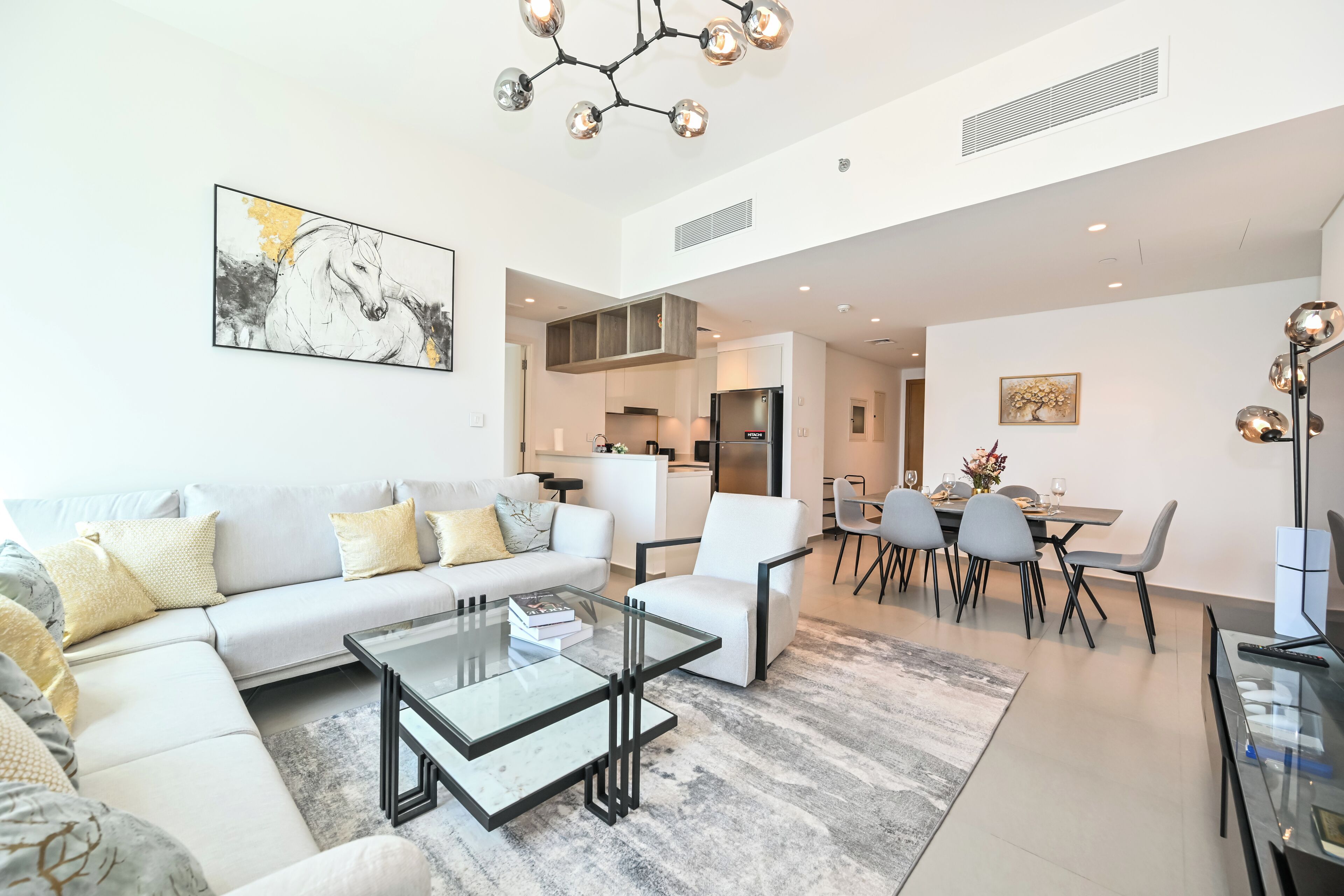A modern living room with a sectional sofa, a glass coffee table, and a dining area with a chandelier.