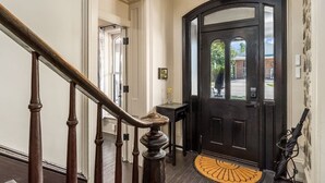 A black door with a glass panel, a wooden staircase, and a small table with a vase.