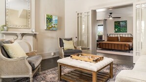 A living room with a large mirror, two chairs, a coffee table, and a bed in the background.