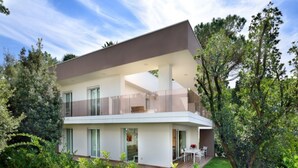 Ein modernes, zweistöckiges Haus mit Balkon, umgeben von üppigem Grün.