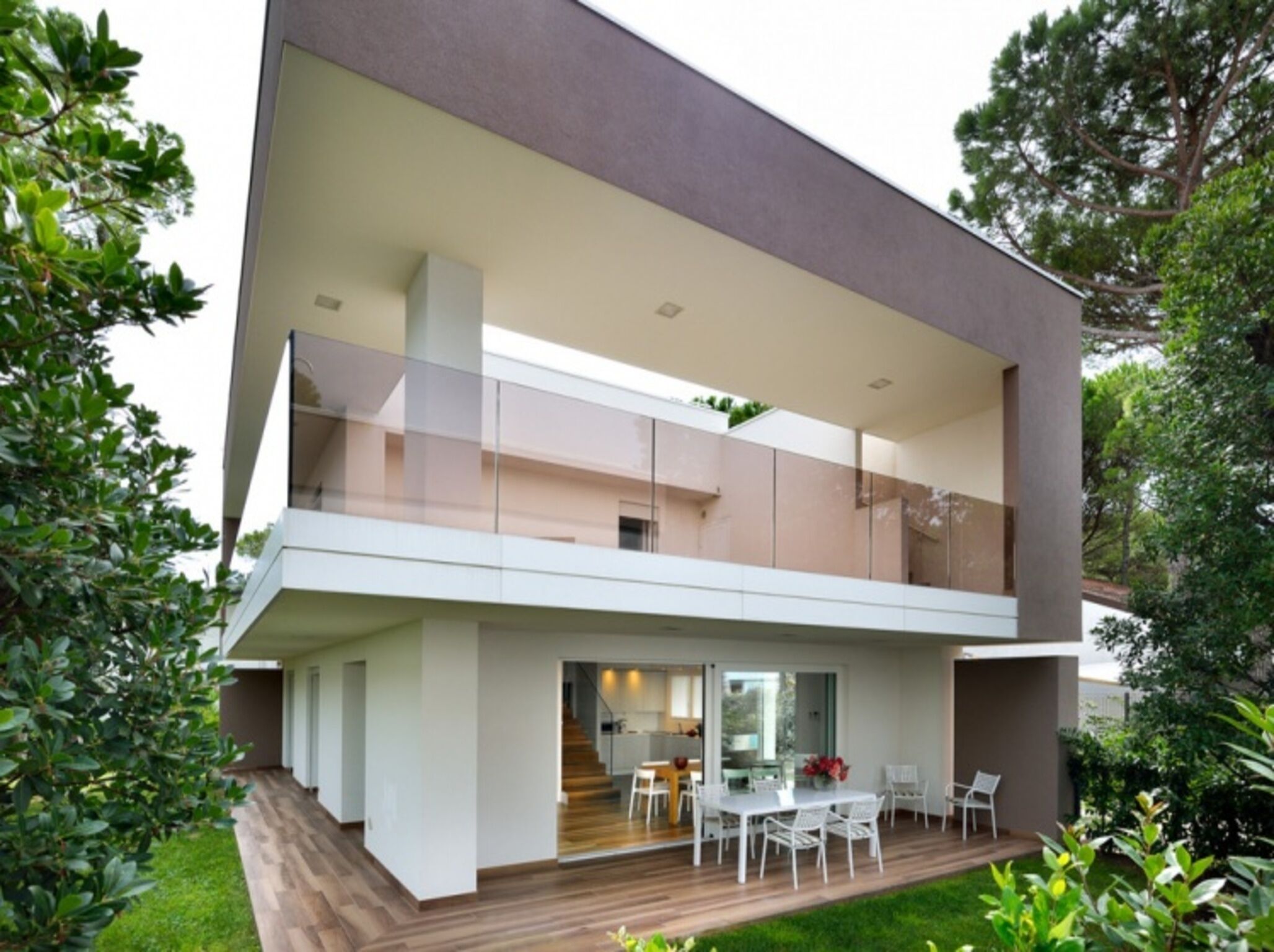Ein modernes, zweistöckiges Haus mit flachem Dach, großen Glasfenstern und einer Holzterrasse.