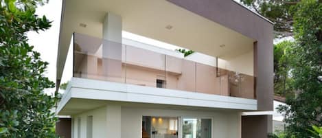 A modern two-story house with a flat roof, large glass windows, and a wooden deck.