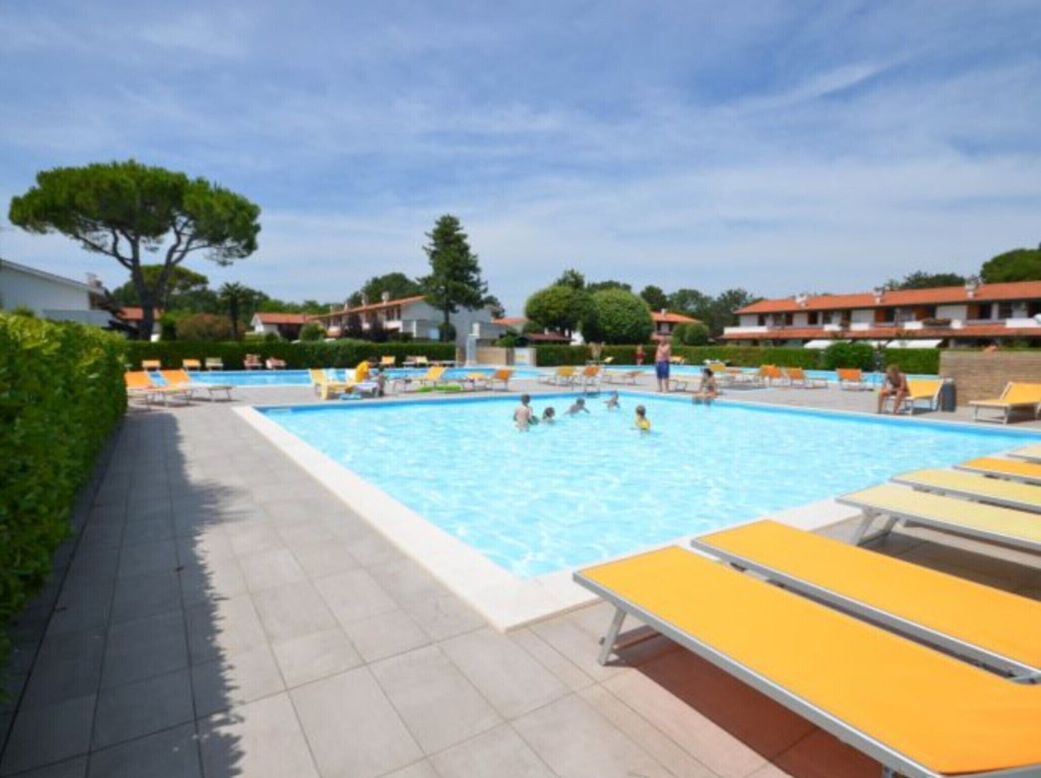 A swimming pool with yellow sun loungers, surrounded by greenery and buildings.