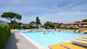 Una piscina con tumbonas amarillas, rodeada de vegetación y edificios.