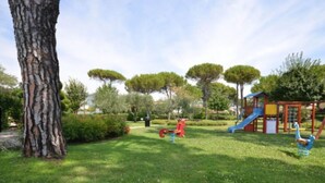 Un parque infantil con toboganes y columpios, rodeado de césped y árboles.